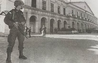 Foto em preto e branco de homem ao lado de um prédio

Descrição gerada automaticamente